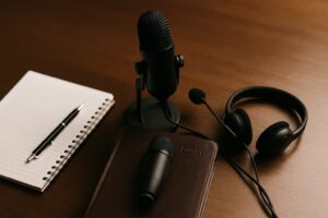 Microfone, fones de ouvido, Bíblia e caderno sobre a mesa, simbolizando a gravação de devocionais em áudio com apoio de inteligência artificial.