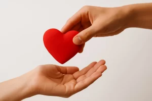 Duas mãos interagindo; uma entrega um coração vermelho à outra, simbolizando amor, perdão e restauração cristã.